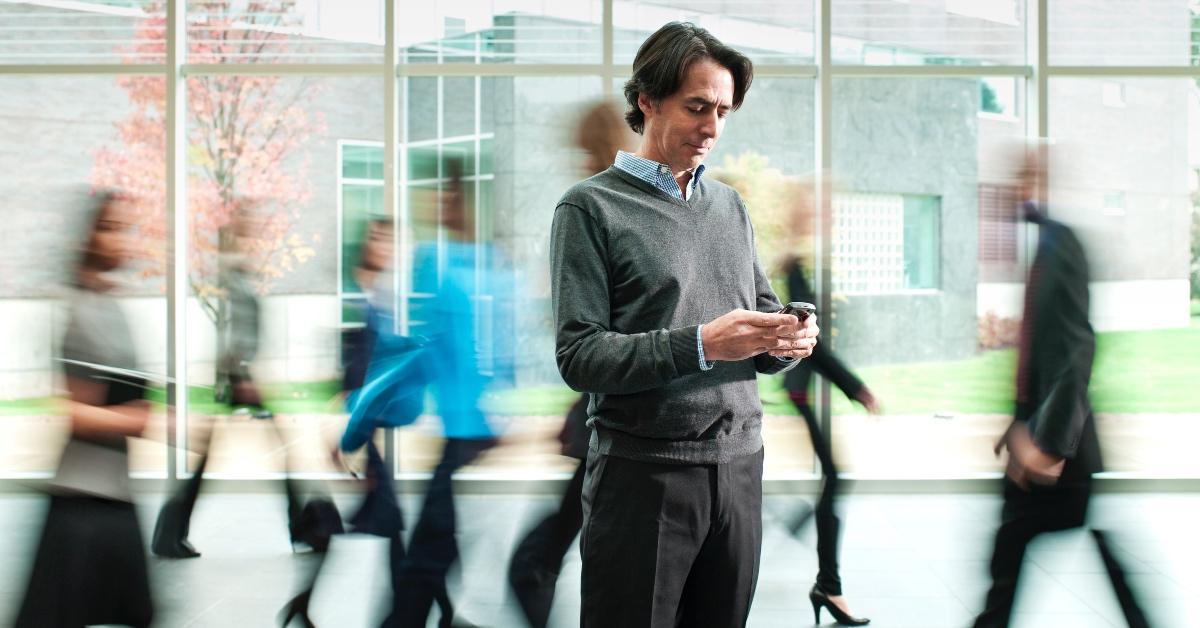 Man on his phone while others around him pass him by.