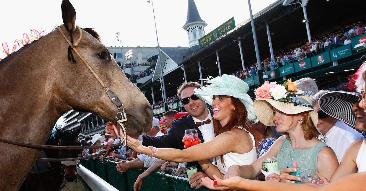 A woman in a fancy hat pets a horse