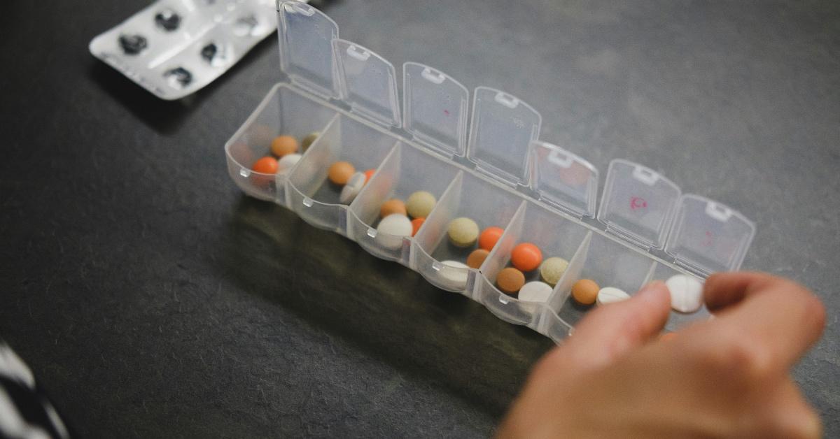 Person putting multi-colored pills in a clear plastic pill box. 