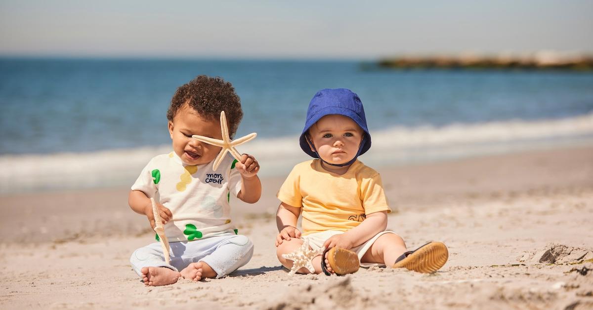 Two babies sit on a beach playing with starfish toys