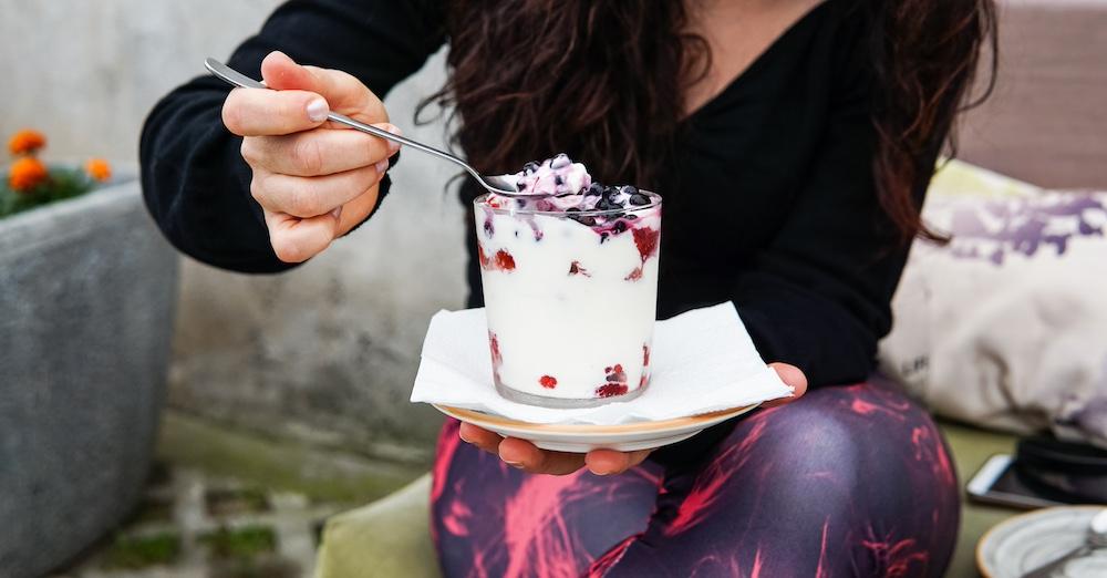 Someone sitting and eating Greek yogurt with a mix of fruit.