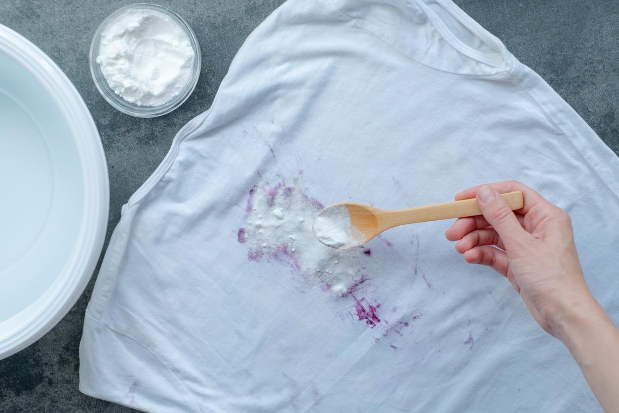 Overhead view of baking soda being sprinkled onto a dark colored stain with a wooden spoon.