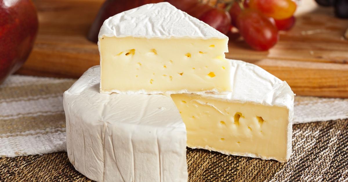 Wheel of brie cheese on a brown tabletop with a slice cut out of it