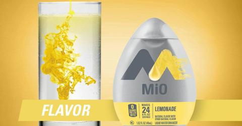 A glass of water with lemonade flavored MiO next to a bottle of Lemonade MiO in front of a yellow background with a yellow banner reading "Flavor" in white letters in the bottom center.