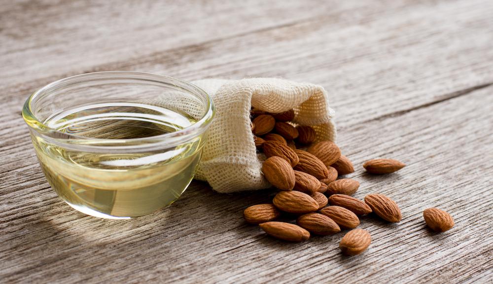 Almond oil in bowl and almonds in muslin bag on wooden table