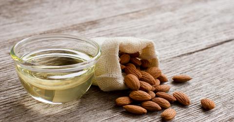 Almond oil in bowl and almonds in muslin bag on wooden table
