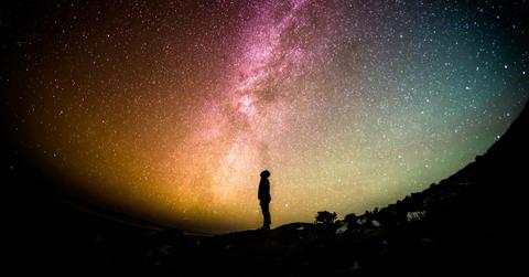 A black silhouette of a man looks up at the Milky Way