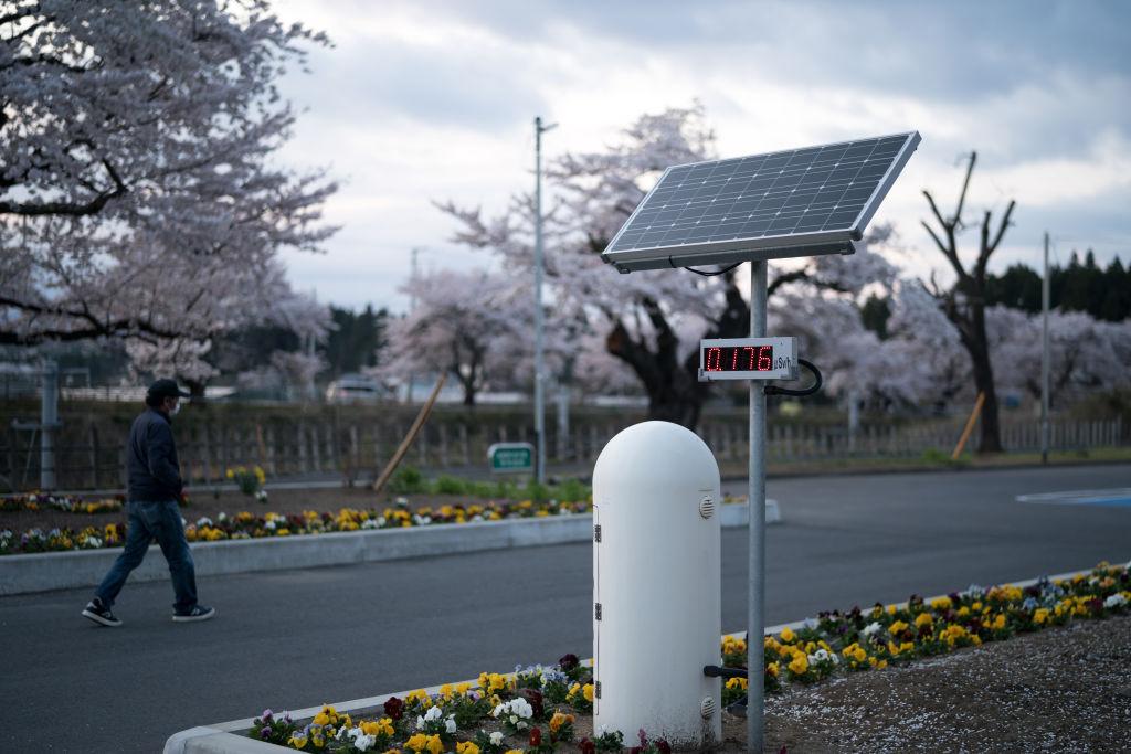 Person walking in Fukushima after evacuation order was lifted. Photo focuses on a radiation monitoring post