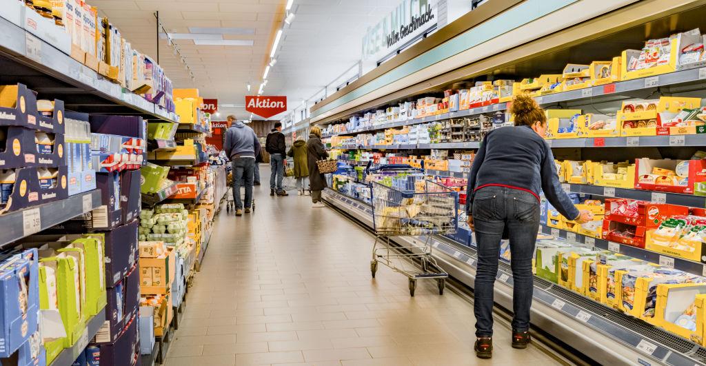 Shoppers in an Aldi store are pictured throughout a mixed aisle of refrigerated and shelf-stable goods.