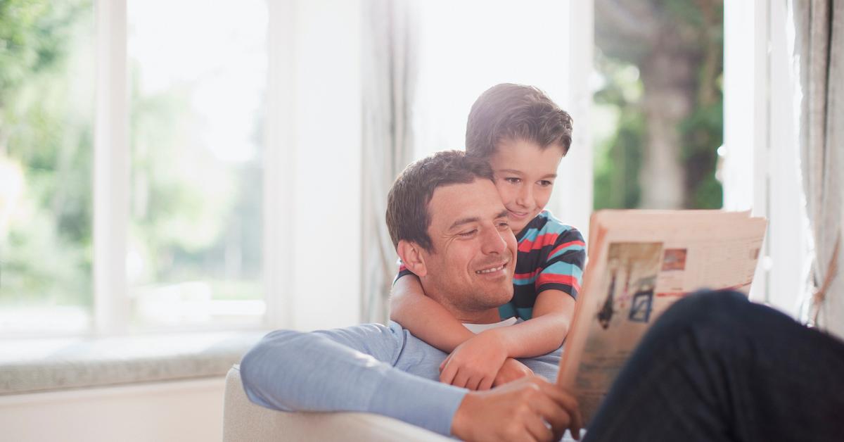 Father and son sitting in a living room reading a newspaper. 