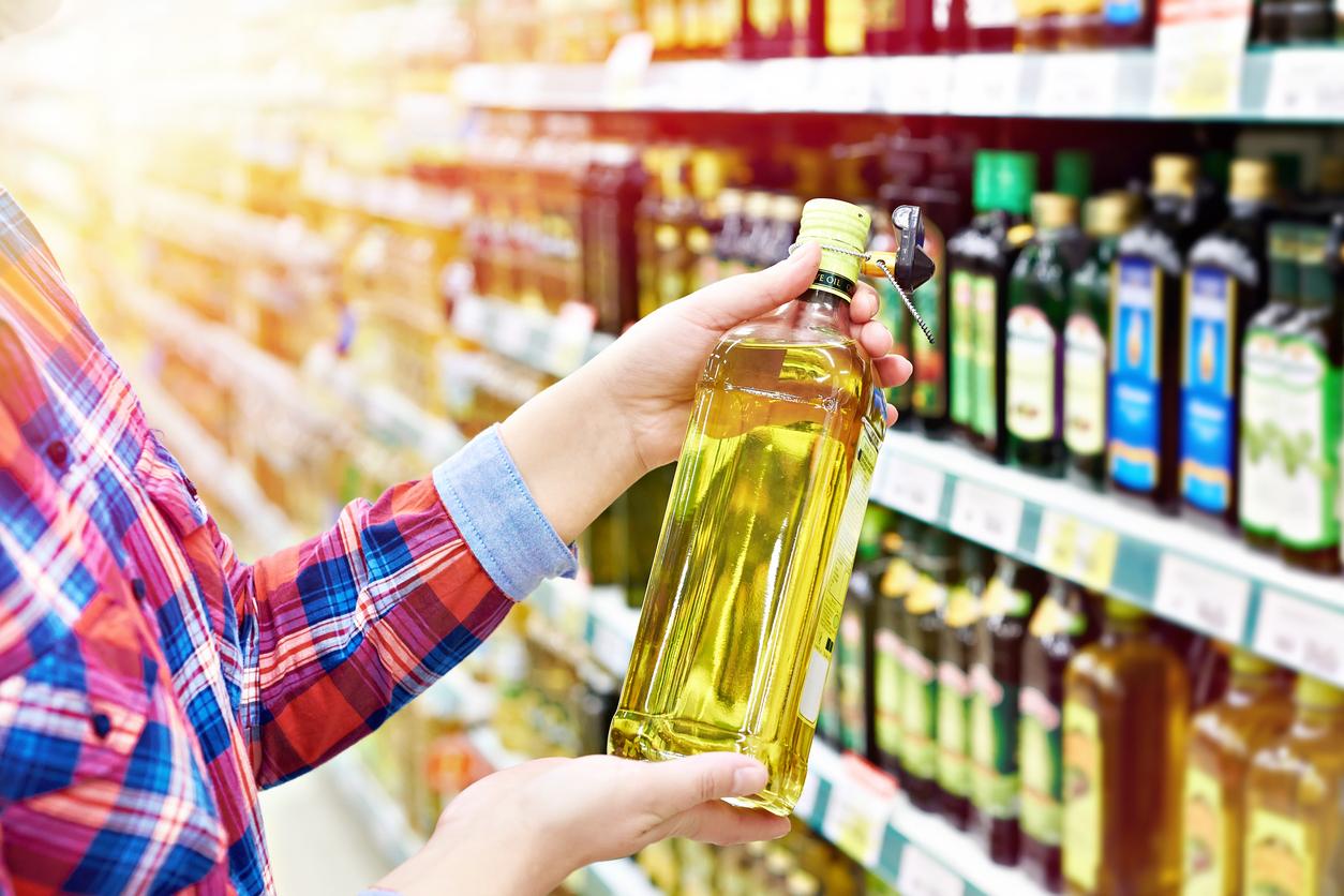 A customer picks up a bottle of olive oil in an oil aisle in a grocery store. 