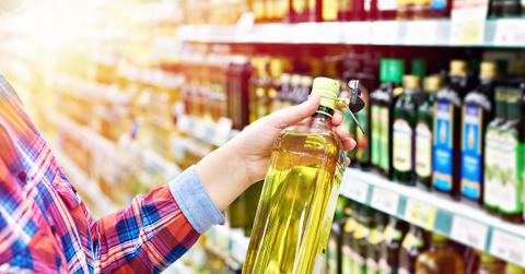 A customer picks up a bottle of olive oil in an oil aisle in a grocery store.