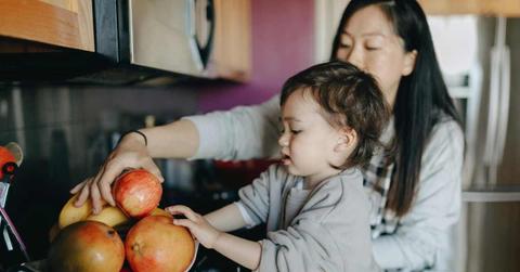 A mom and her son storing apples and other fruits in a bowl on the kitchen counter. (Representative Cover Image Source: Pexels | PNW Production)