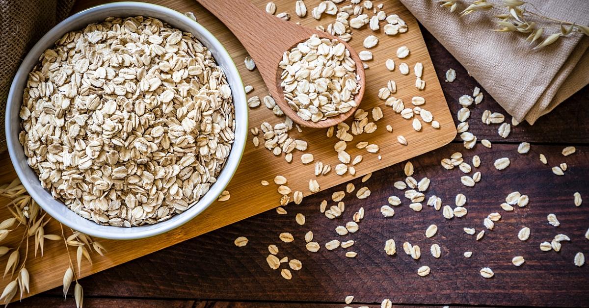 Photo of a bowl of oat flakes sitting on a cutting board with flakes spread across the wooden surface