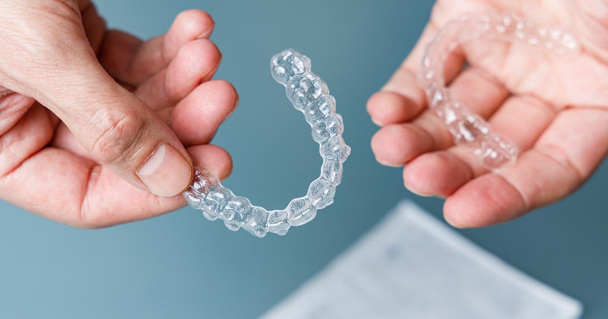 Hands holding transparent aligners on blue background