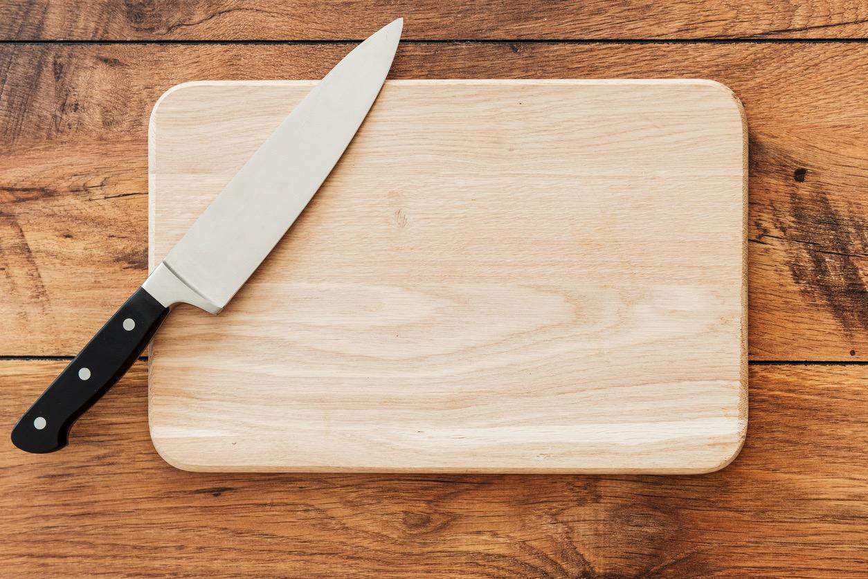 A straight-on view of a clean wood cutting board and a kitchen knife on a table. 