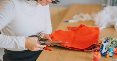 A crafter uses scissors to cut into orange fabric scraps.
