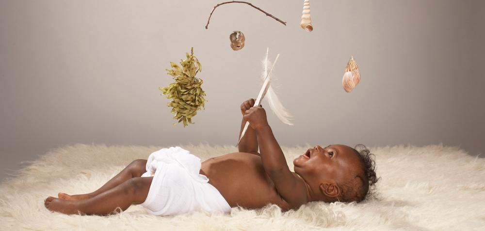 A baby lays on a white rug and plays with a mobile.