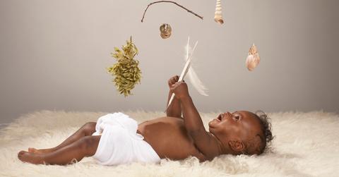 A baby lays on a white rug and plays with a mobile.