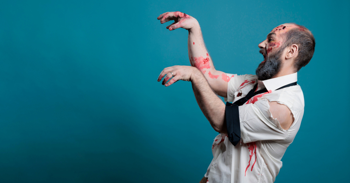 A man in ripped clothes and covered in fake blood pretends to be a zombie 