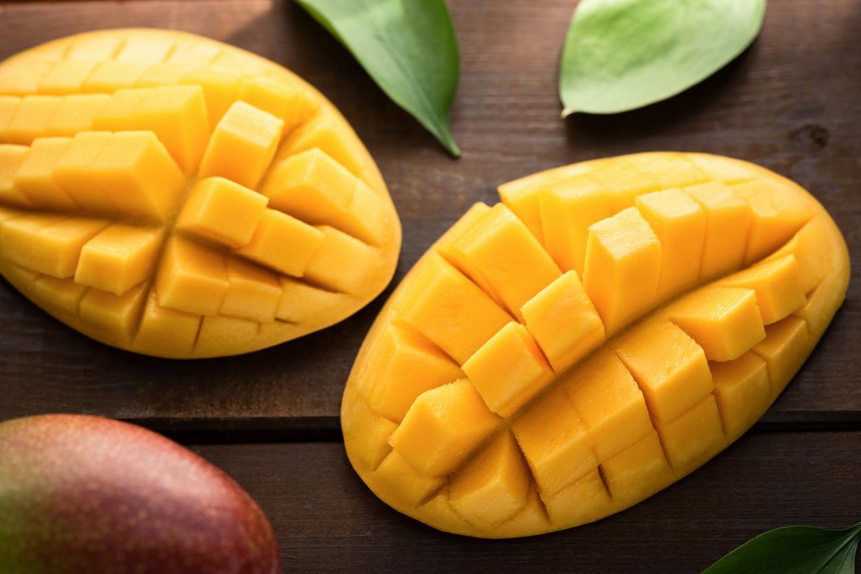 Two mangoes are pictured cut open, with their insides artistically cut into several pieces atop a wooden table.