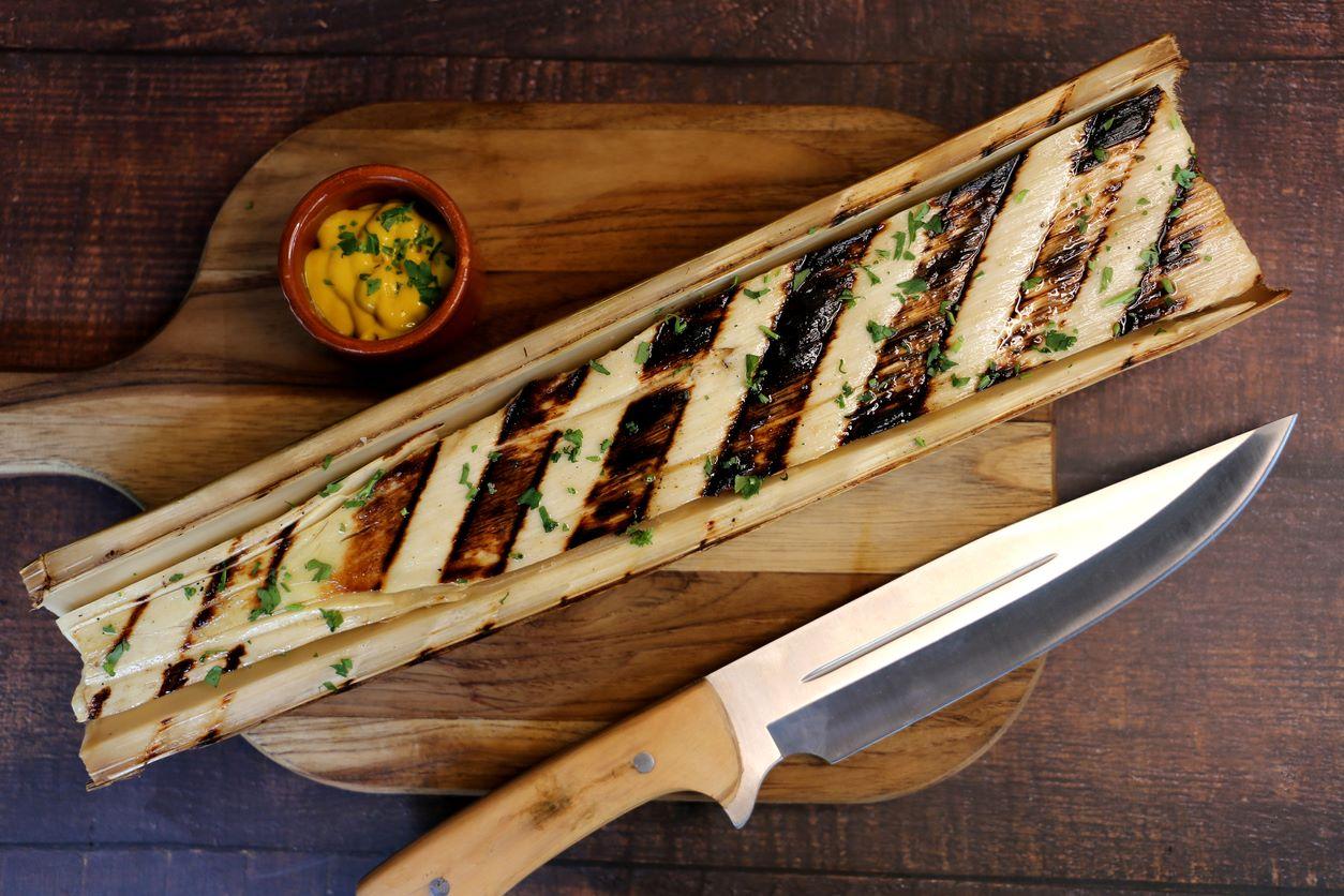 Grilled whole hearts of palm with barbeque marks on a wooden board with knife