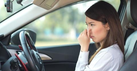 A woman plugs her nose due to the offensive smell inside her car.