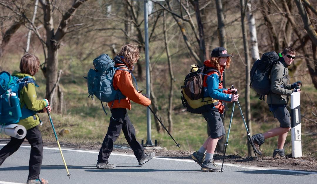 A group of teenagers crossing a road with hiking gear 