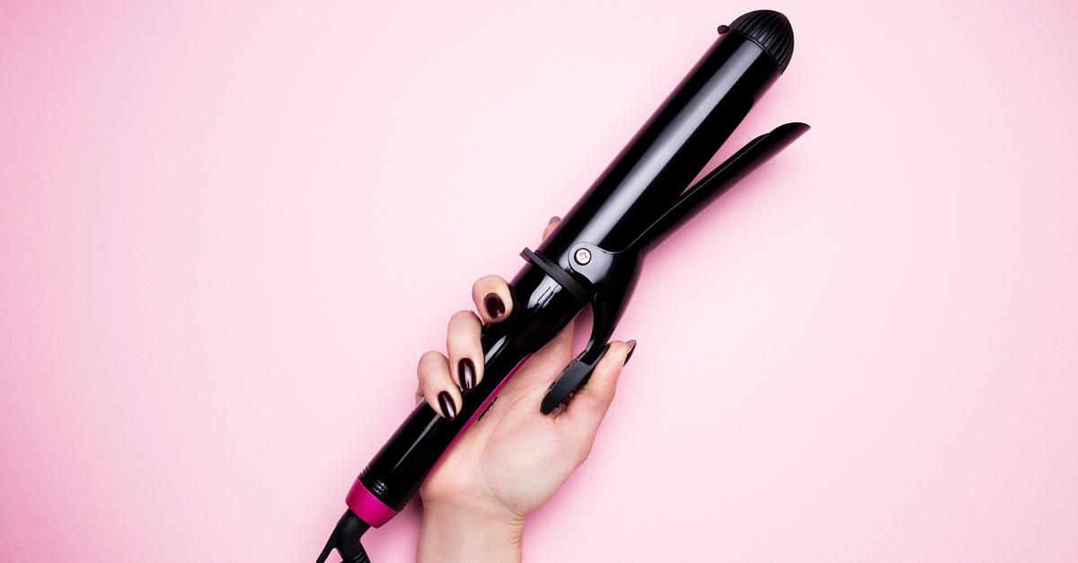 hand holding a curling iron on pink bckground