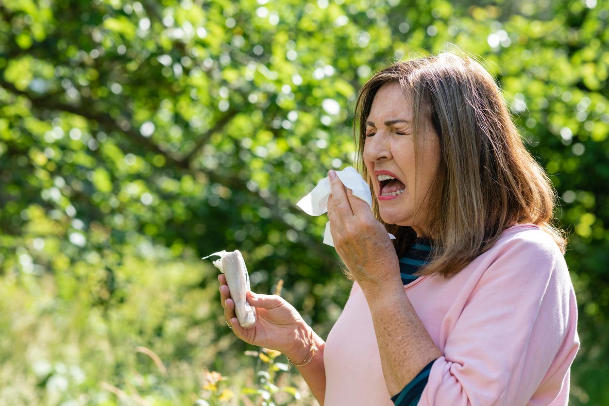 A woman sneezing into a tissue outdoors. 