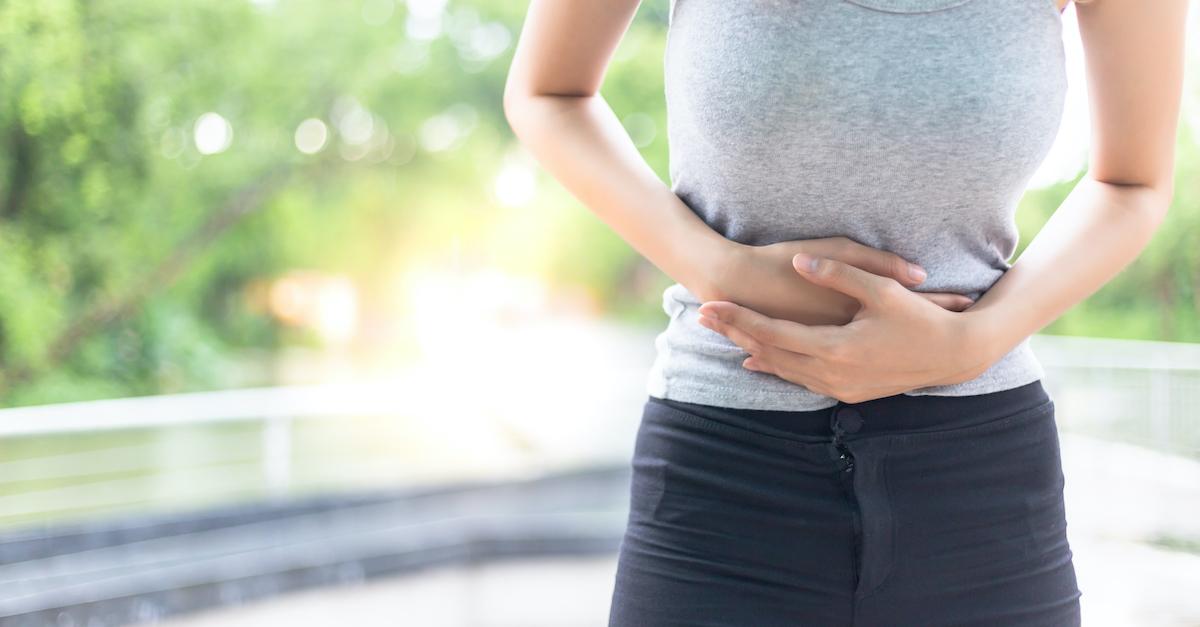 Woman stands outside and holds her stomach