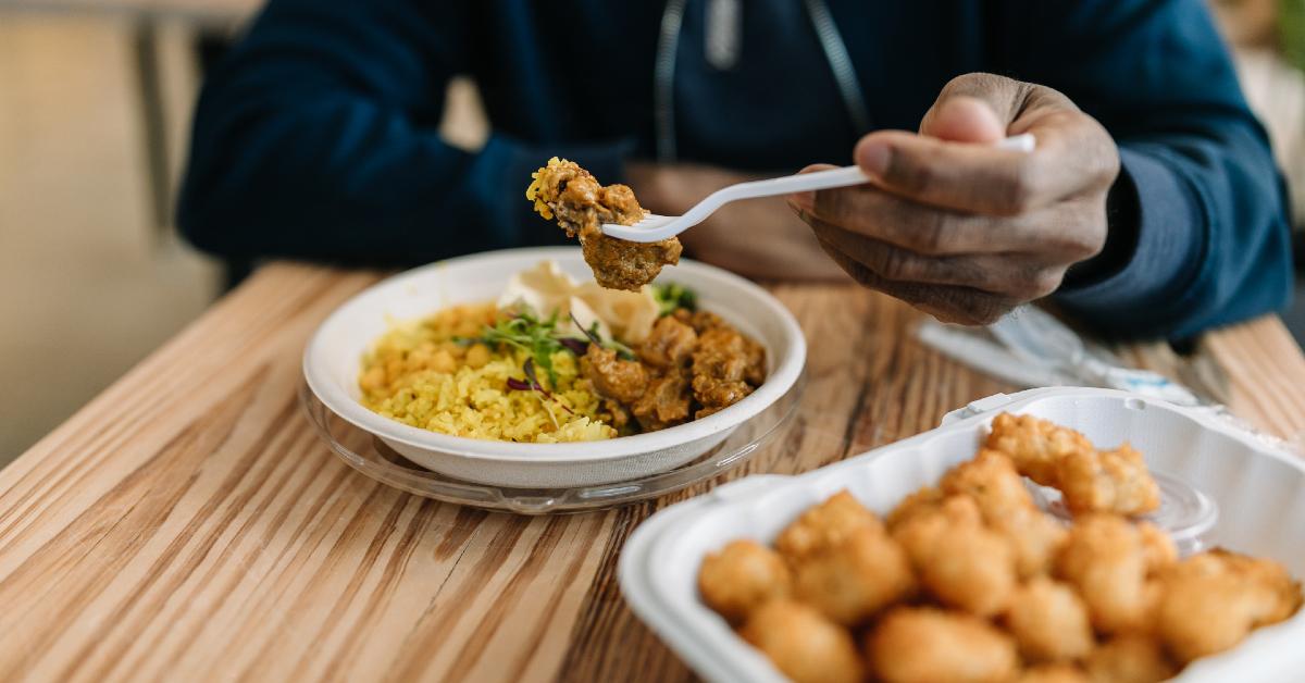 Photo of a Plant Junkie patron eating vegan food from a white bowl at a wooden table