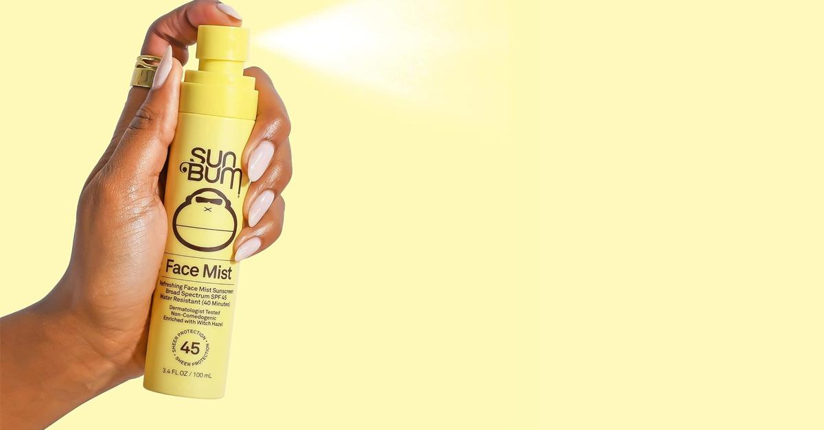 A hand spraying Sun Bum sunscreen on a yellow background