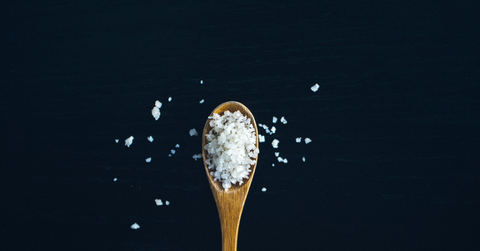 A wooden spoon sits against a black backdrop holding salt grains