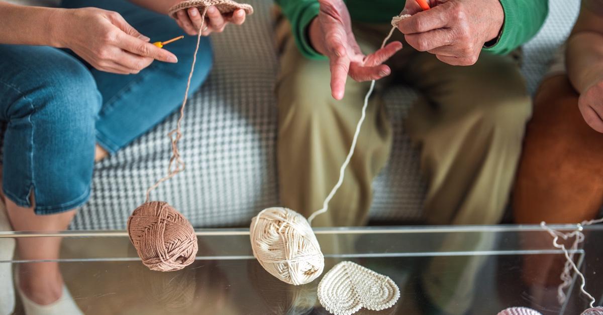 Group of three people sitting on a couch crocheting heart-shaped doilies together. 