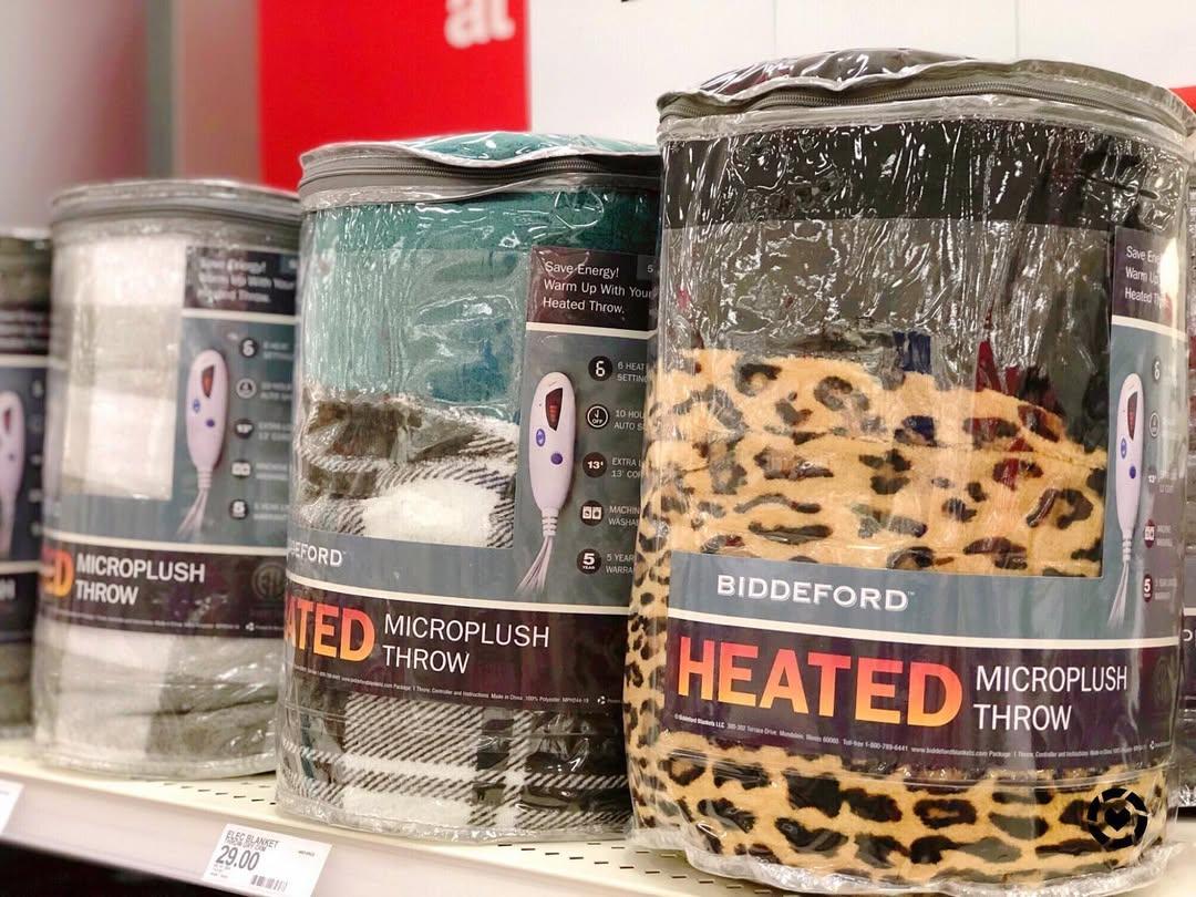 Four blankets from the brand Biddeford are pictured on a Target shelf with the words "Heated Microplush Throw" on the packages.