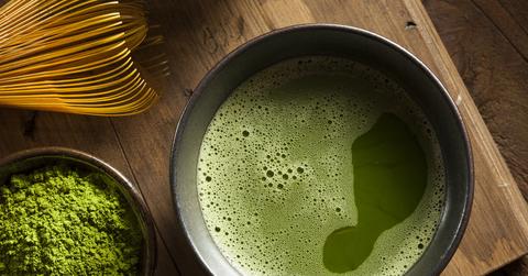 A cup of match sits on a wooden surface next to to a bowl of matcha powder.
