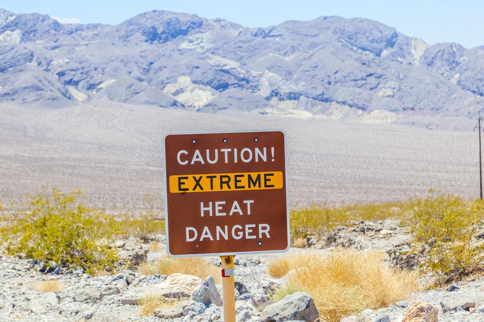 A photo of a sign that reads "Caution! Extreme Heat Danger" in front of Death Valley. 