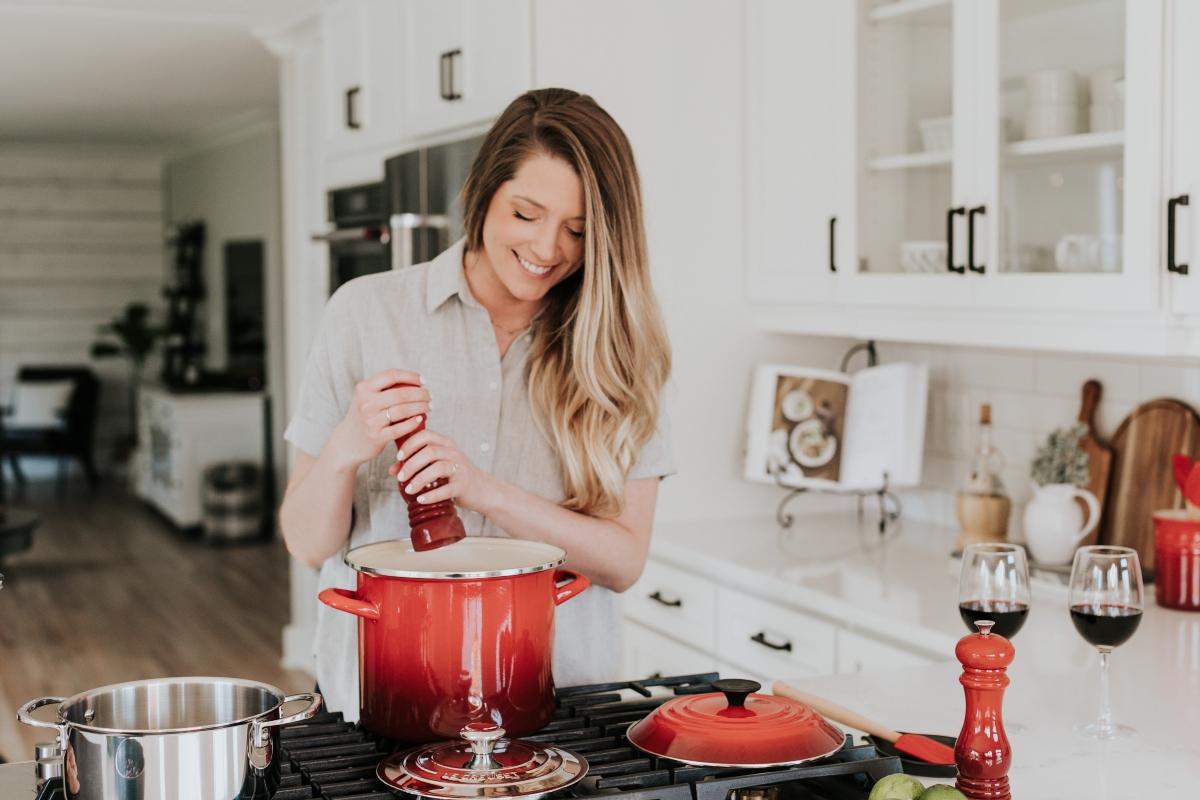 smiling woman cooking in a red pot with two wine glasses next to her