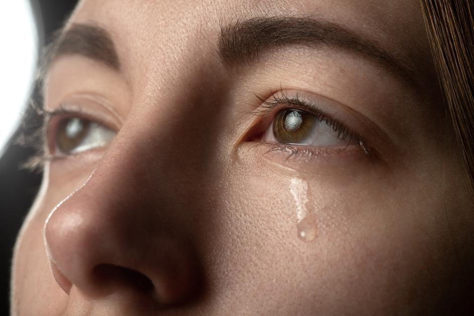 A close up of a person looking up and a tear is coming out of their eyes.