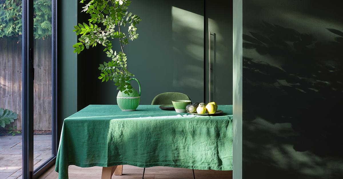 Farrow & Ball dark green paint on a wall with a table covered in a green tablecloth.