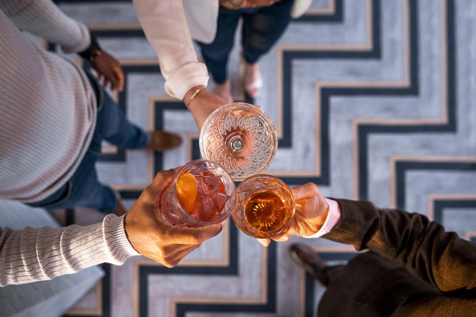 An aerial view of three people holding up their alcoholic drinks together.  