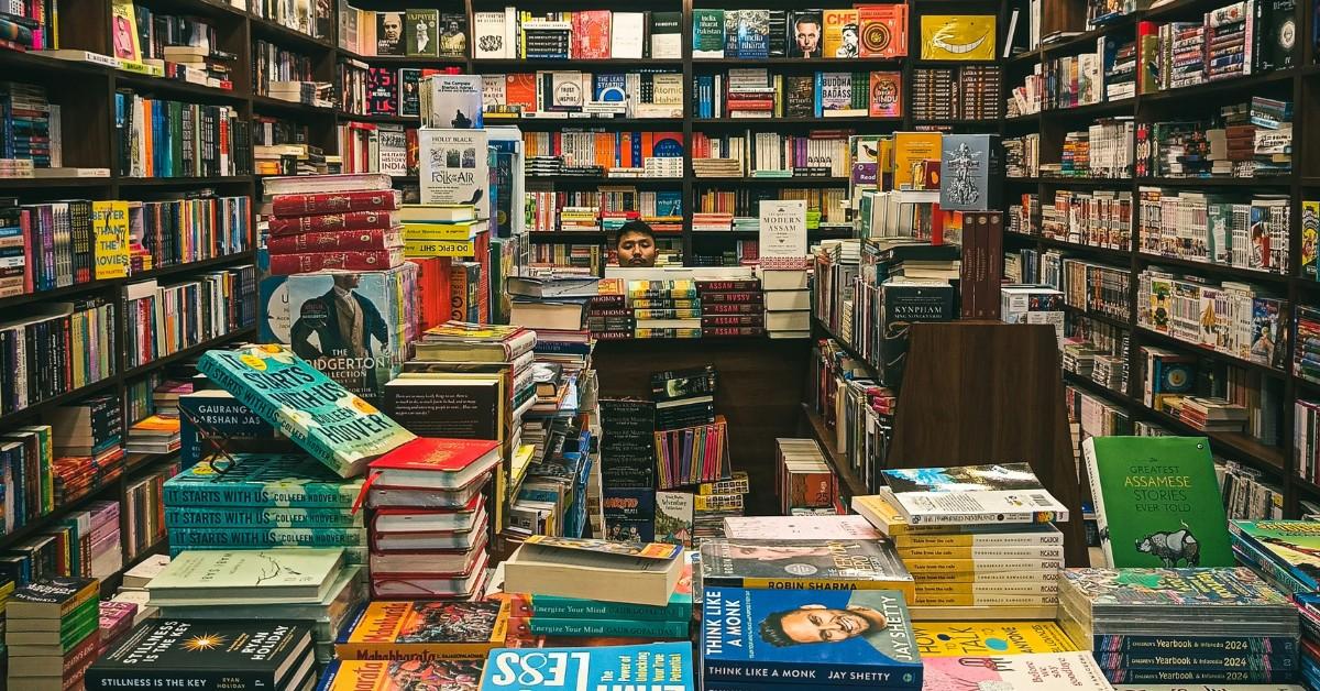 A man peeks out from behind a pile of books in a bookstore 