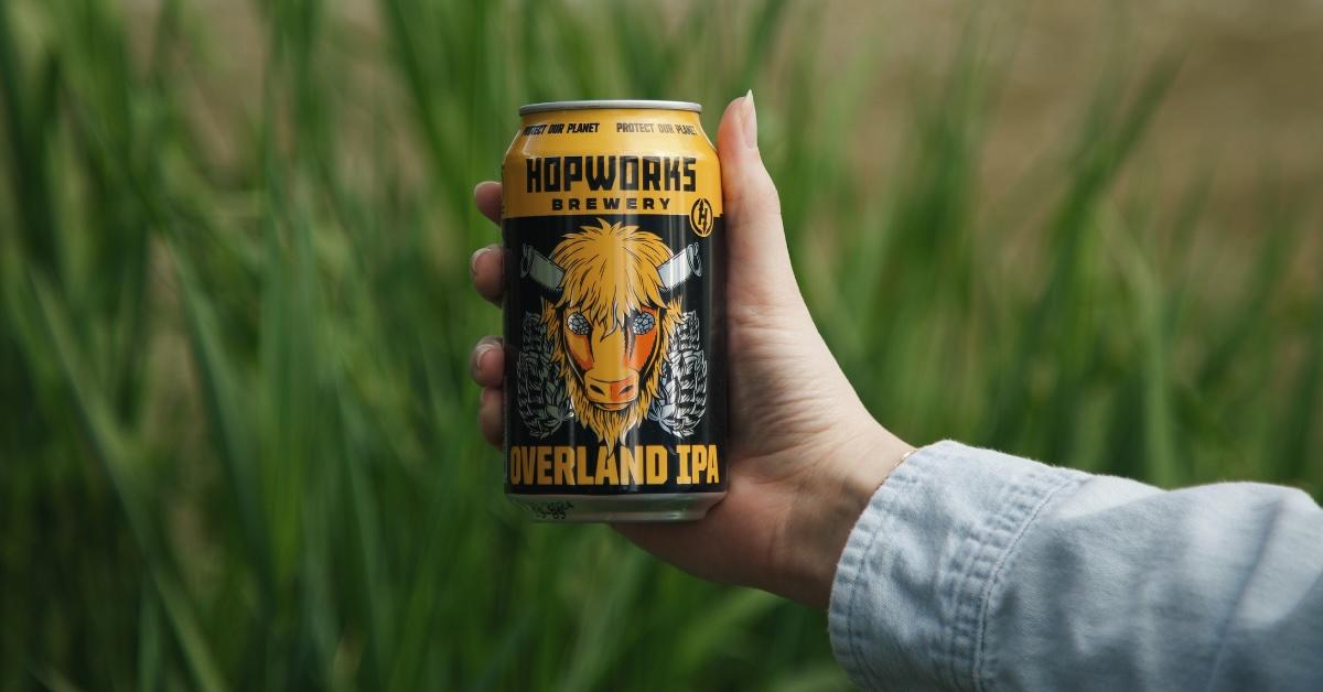 Hand holds a can of Hopworks Brewery Overland IPA in front of tall grass