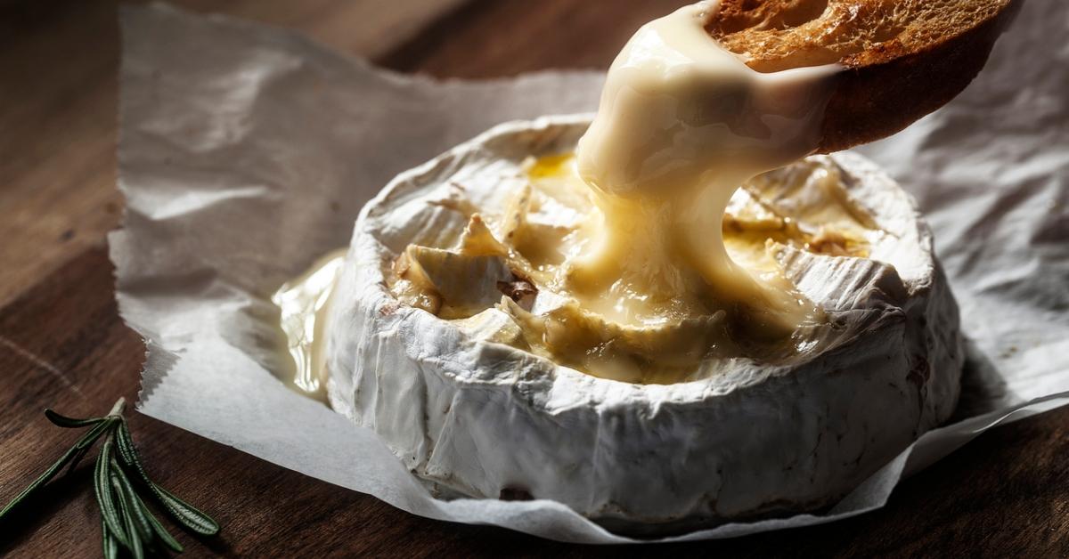 A photo of someone dipping a piece of bread in warm cheese. 