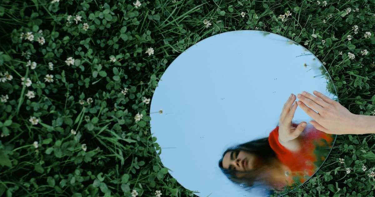 A woman looks at her reflection in a mirror placed in the garden (Representative Cover Image Source: Pexels | Shvets Productions)