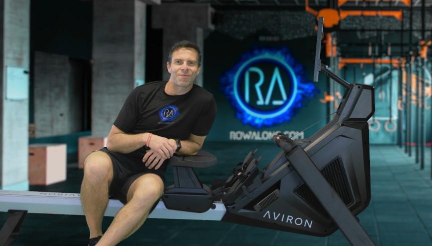 Indoor rowing gold medalist and world record-holder John Steventon sits beside an ergometer.