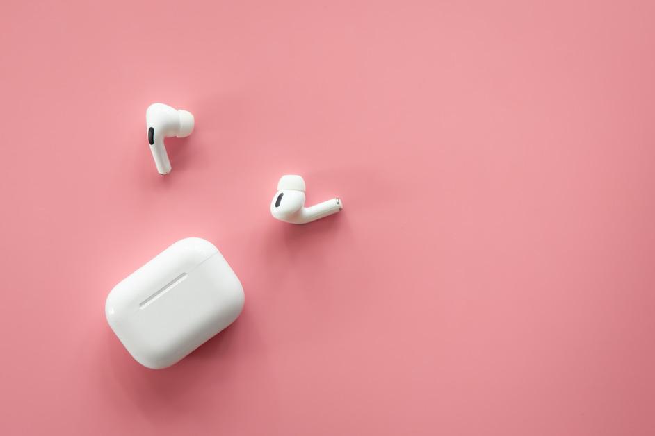 An AirPods case and two lose AirPods Pro earbuds sit in front of a pink background. 