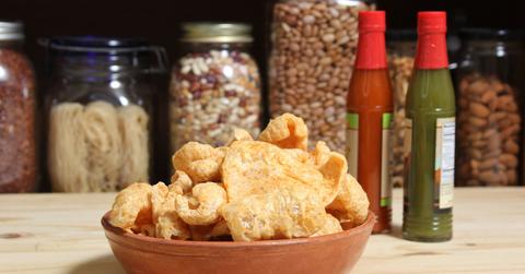Fried pork rinds are served in a wooden bowl beside hot sauce.