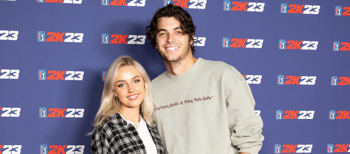 Taylor Fritz and his girlfriend Morgan Riddle smile in front of a PGA TOUR 2K23 backdrop.